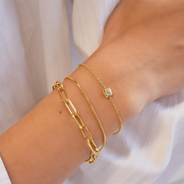 Gold bracelets on a wrist with a plain background