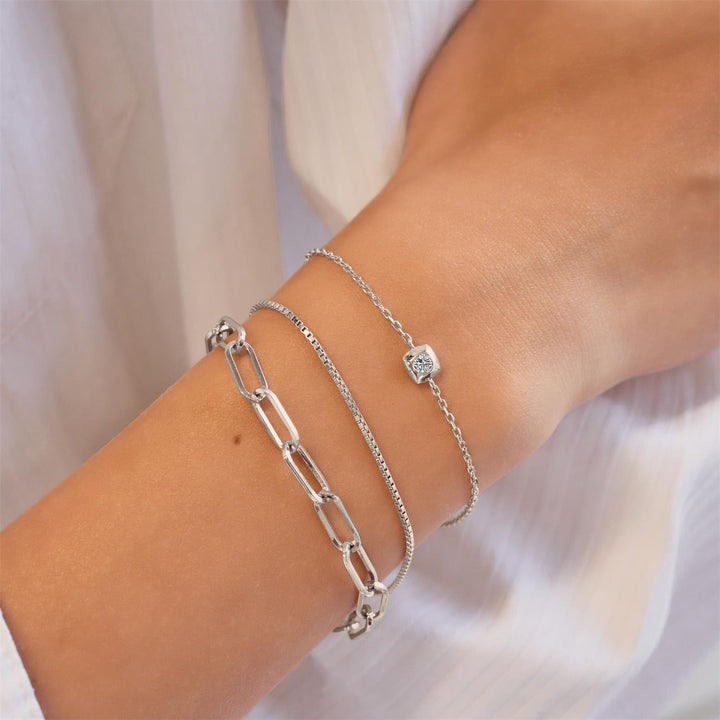 Silver chain bracelets on a wrist with a plain background