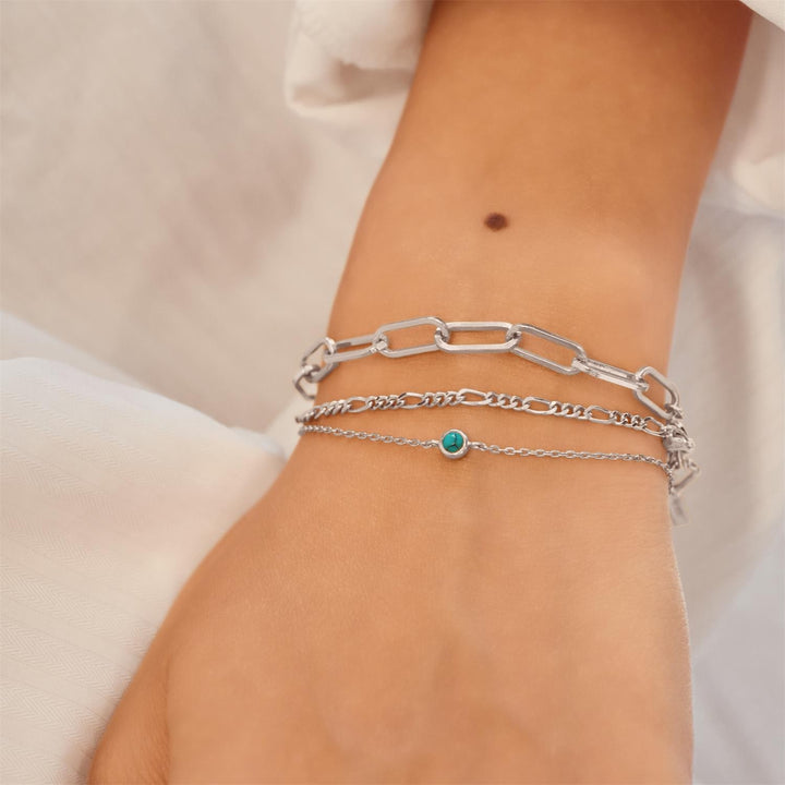 Silver chain bracelets on a wrist with a neutral background