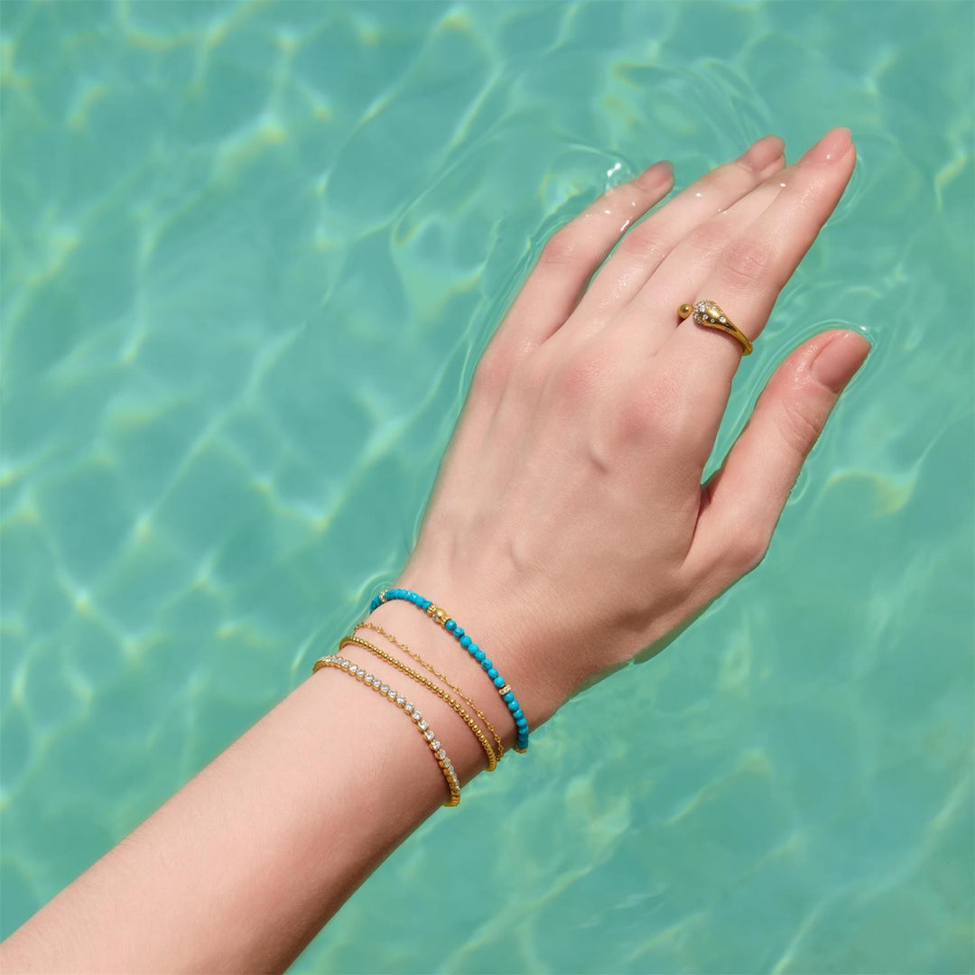 Hand with bracelets and a ring against a turquoise water background
