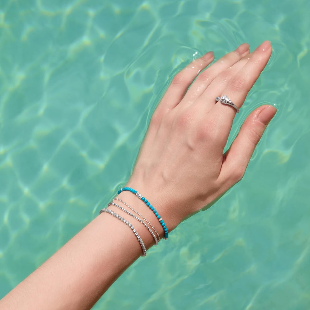 Hand with bracelets and a ring against a turquoise water background