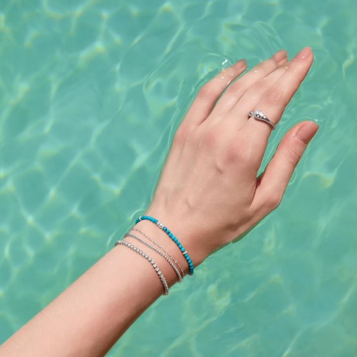 Hand with bracelets and a ring against a turquoise water background