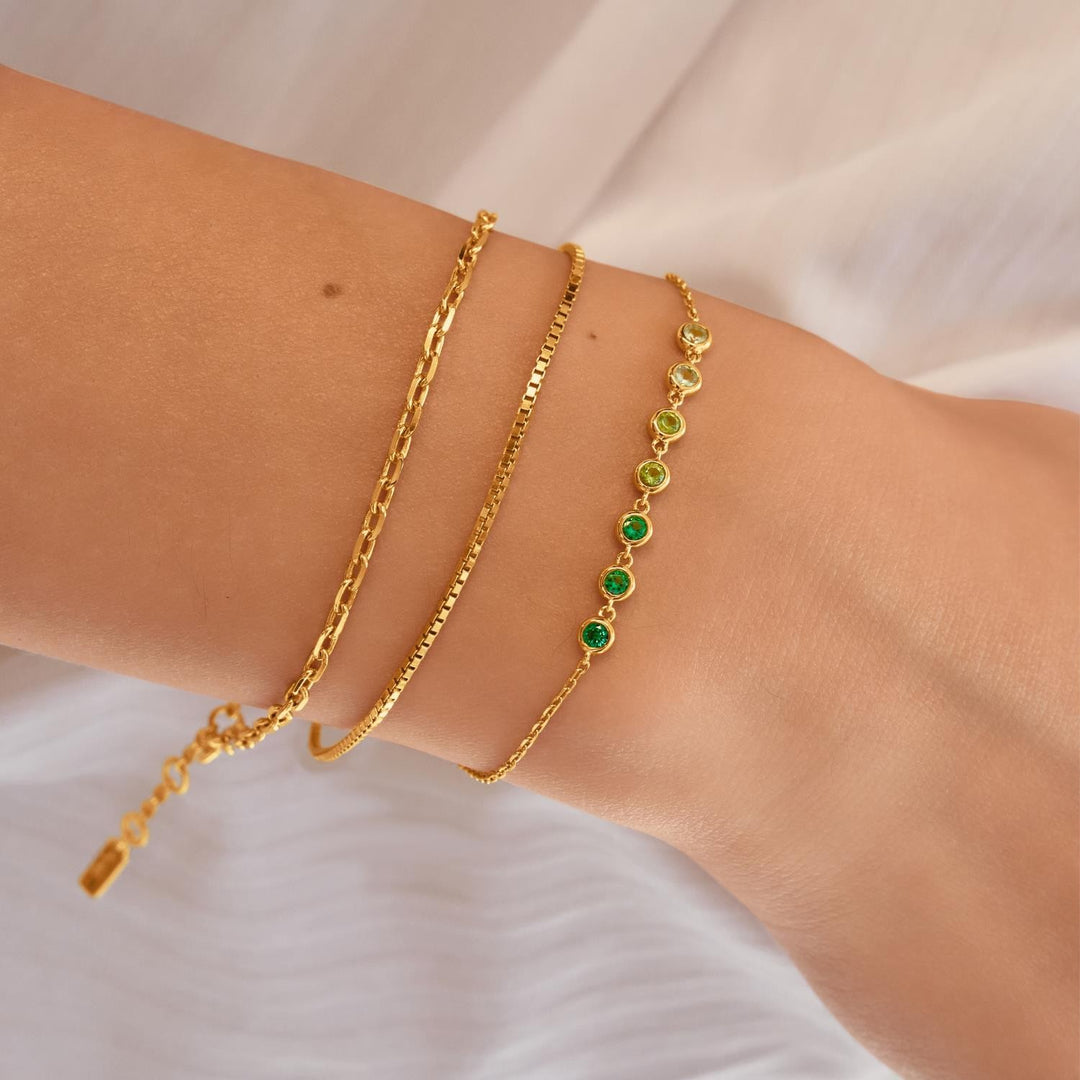 Two gold bracelets on a wrist against a white background
