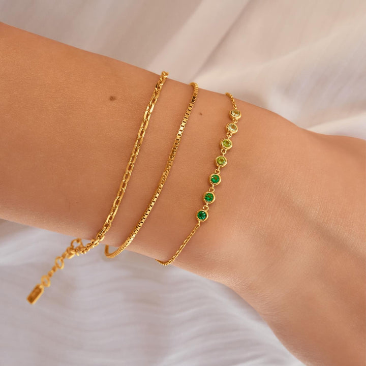 Two gold bracelets on a wrist against a white background