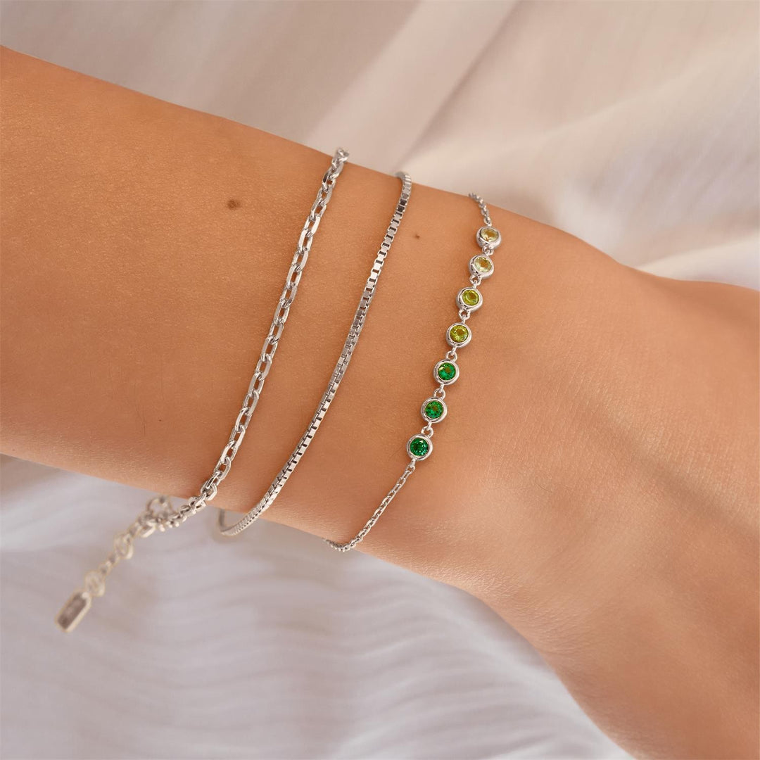 Two silver bracelets with green stones on a wrist against a neutral background