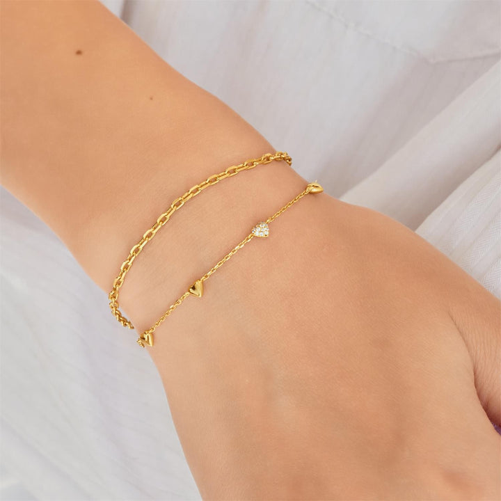 Gold bracelet with heart and triangle charms on a wrist against a white background
