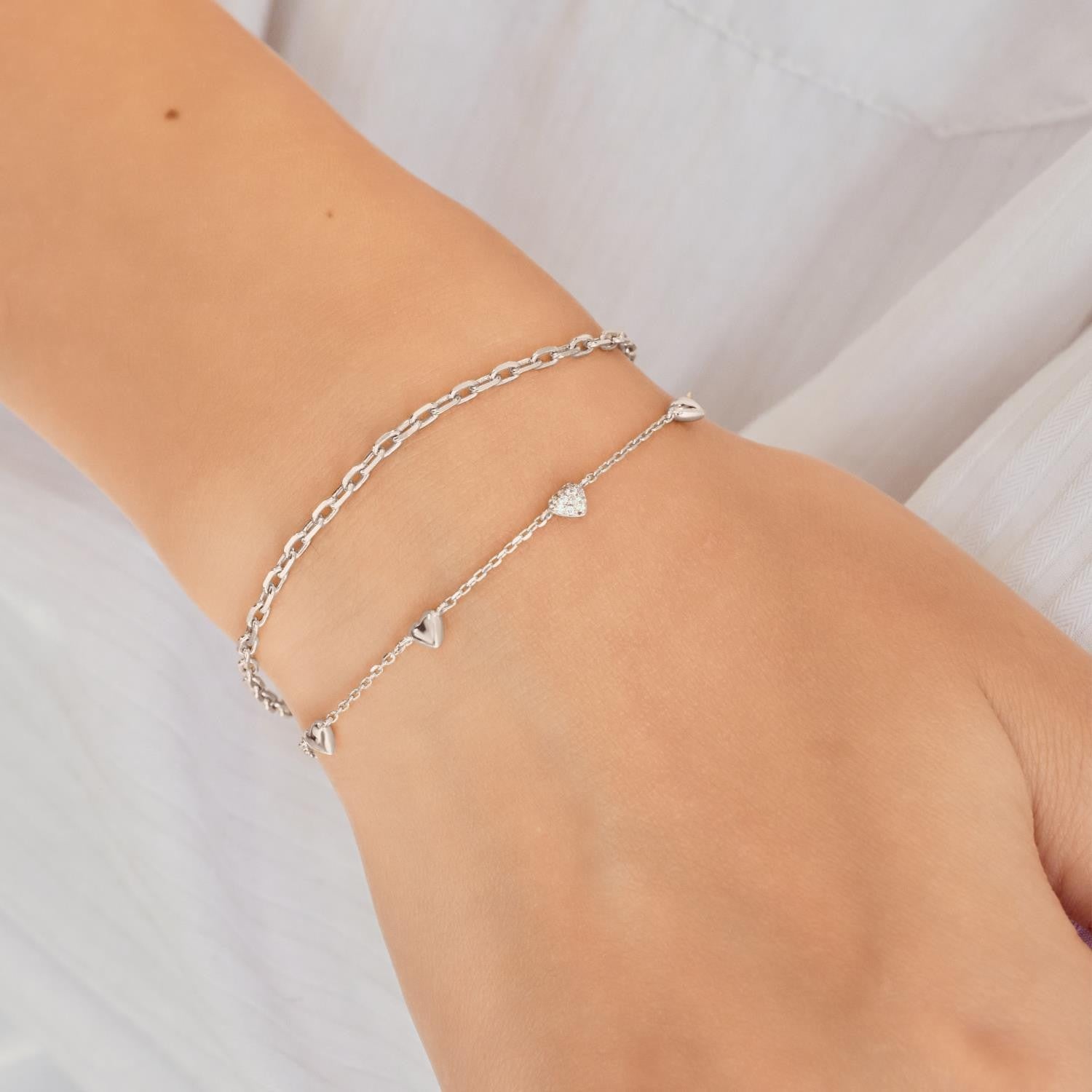 Silver bracelet with heart charms on a wrist against a light background
