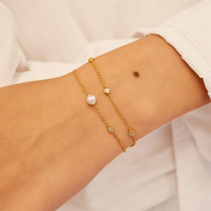 Gold bracelet with pearl and gemstone accents on a wrist against a neutral background