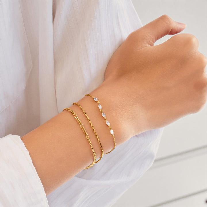 Hand wearing multiple gold bracelets on a white background