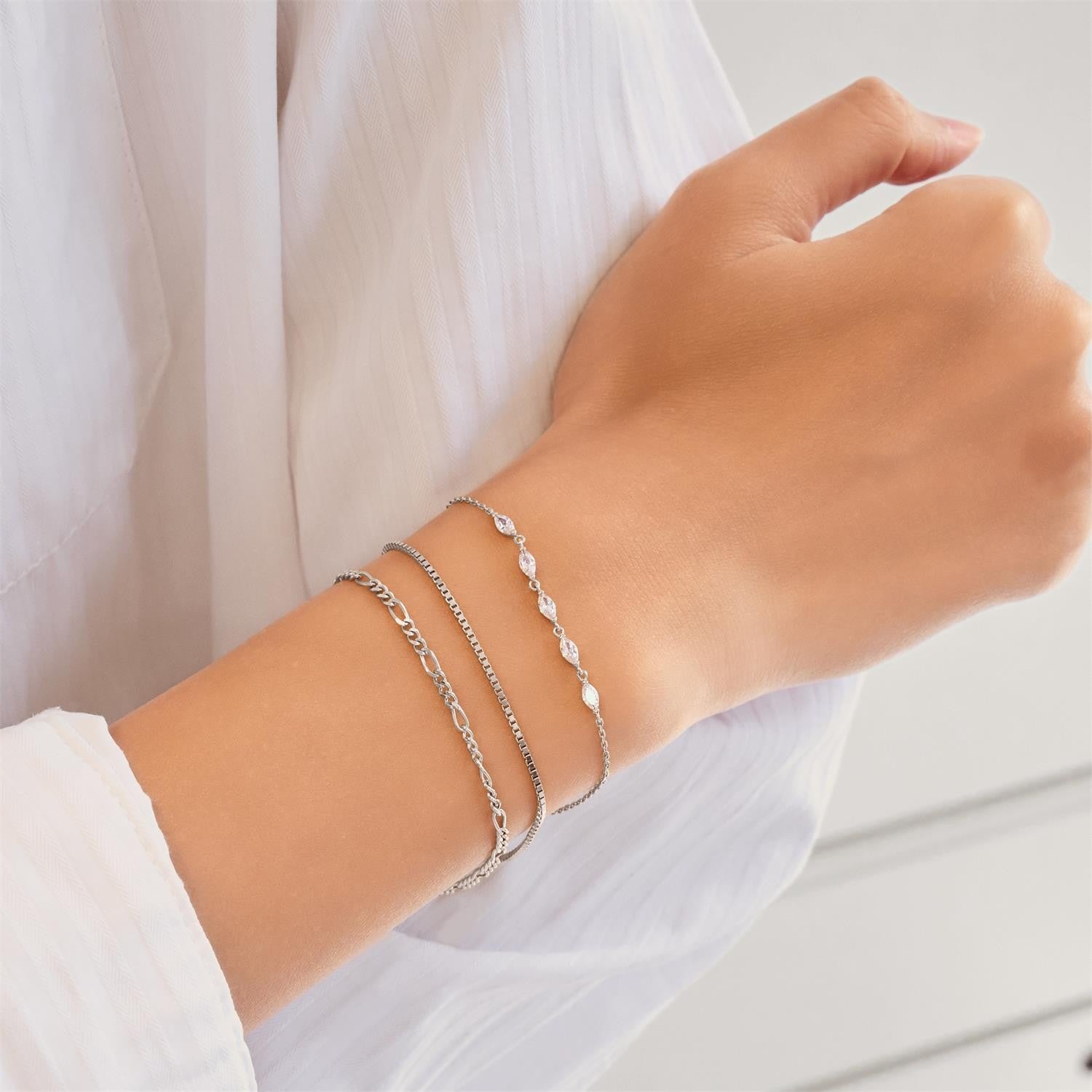 Hand wearing multiple silver bracelets on a white background