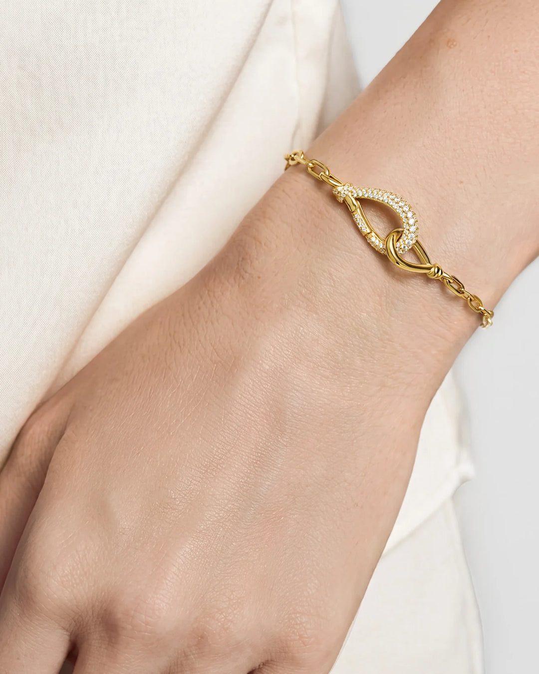 A close-up of a delicate gold chain bracelet with a pavé-set oval clasp, shown worn on a person's wrist.