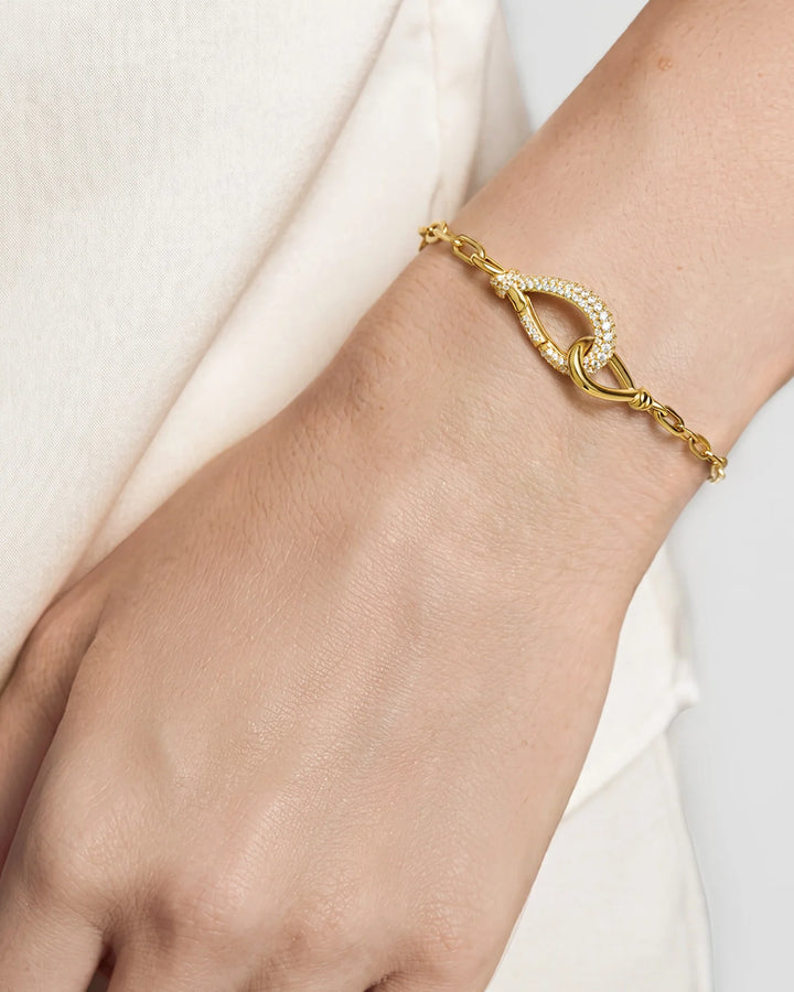 A close-up of a delicate gold chain bracelet with a pavé-set oval clasp, shown worn on a person's wrist.