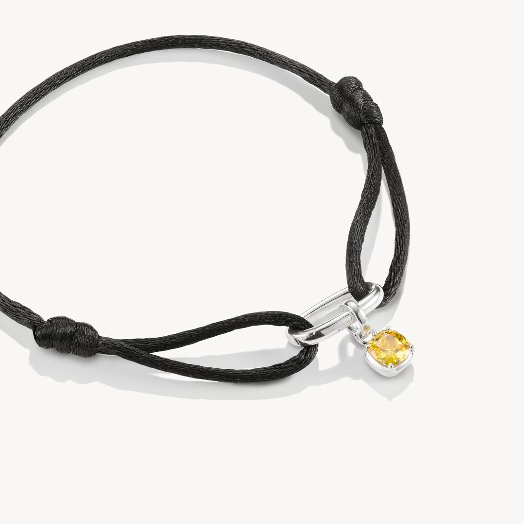 Bracelet with a yellow gemstone charm on a black cord against a white background