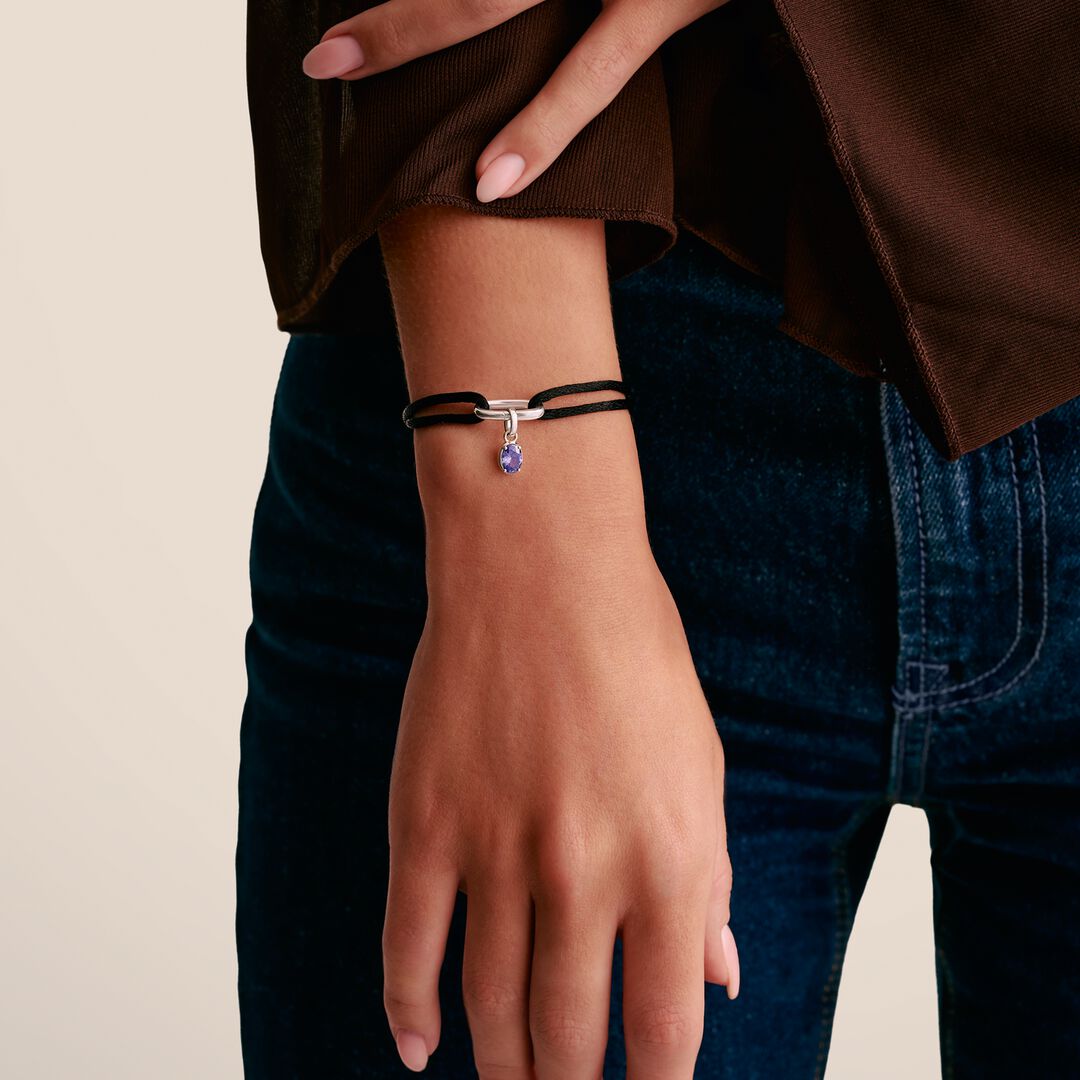 Person wearing a bracelet with a purple charm on a neutral background