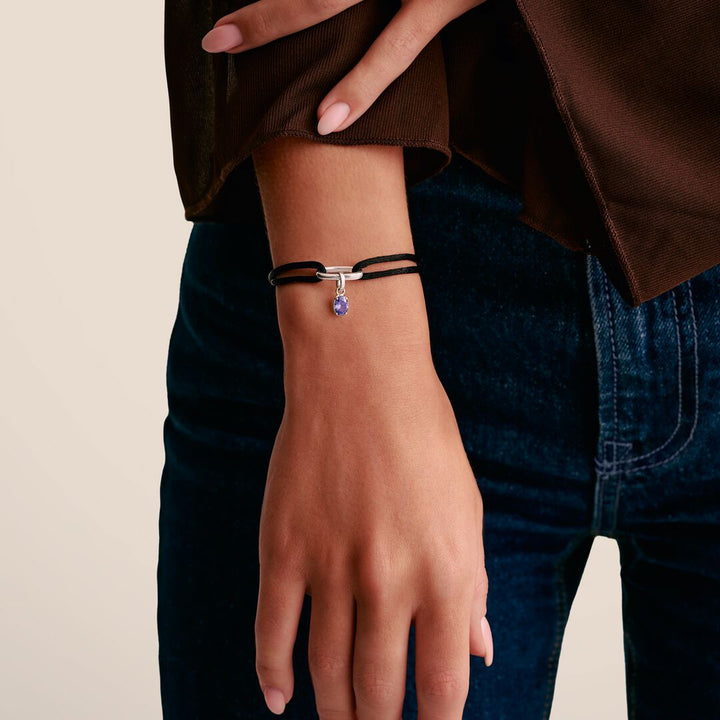 Person wearing a bracelet with a purple charm on a neutral background
