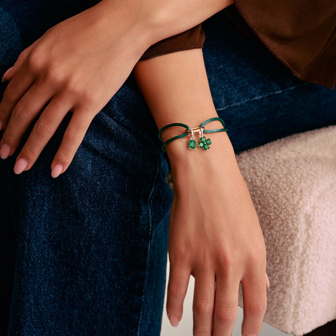 Close-up of a hand wearing a green bracelet with small charms on a neutral background
