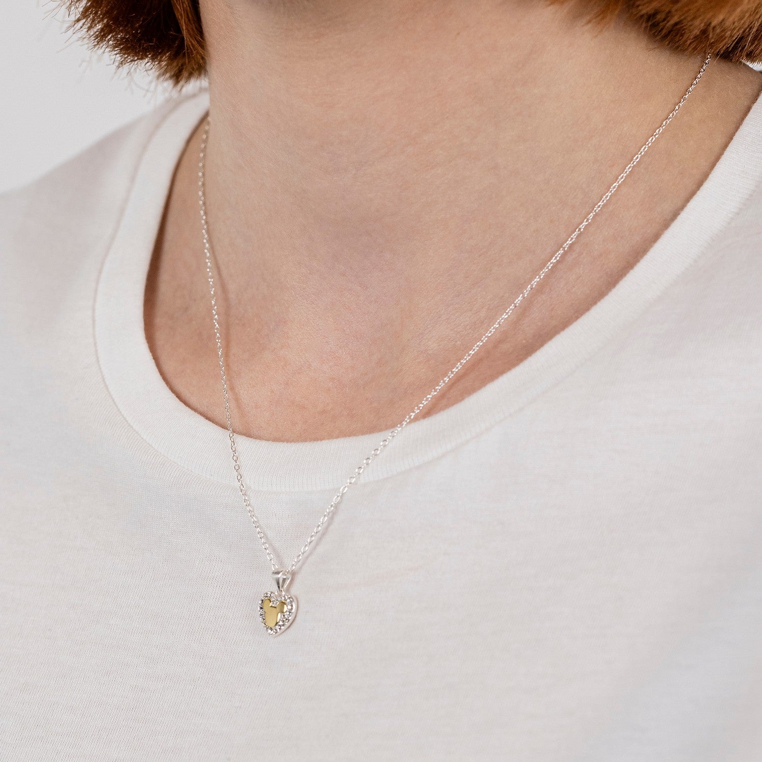 Silver necklace with a heart-shaped pendant worn by a person on a white background
