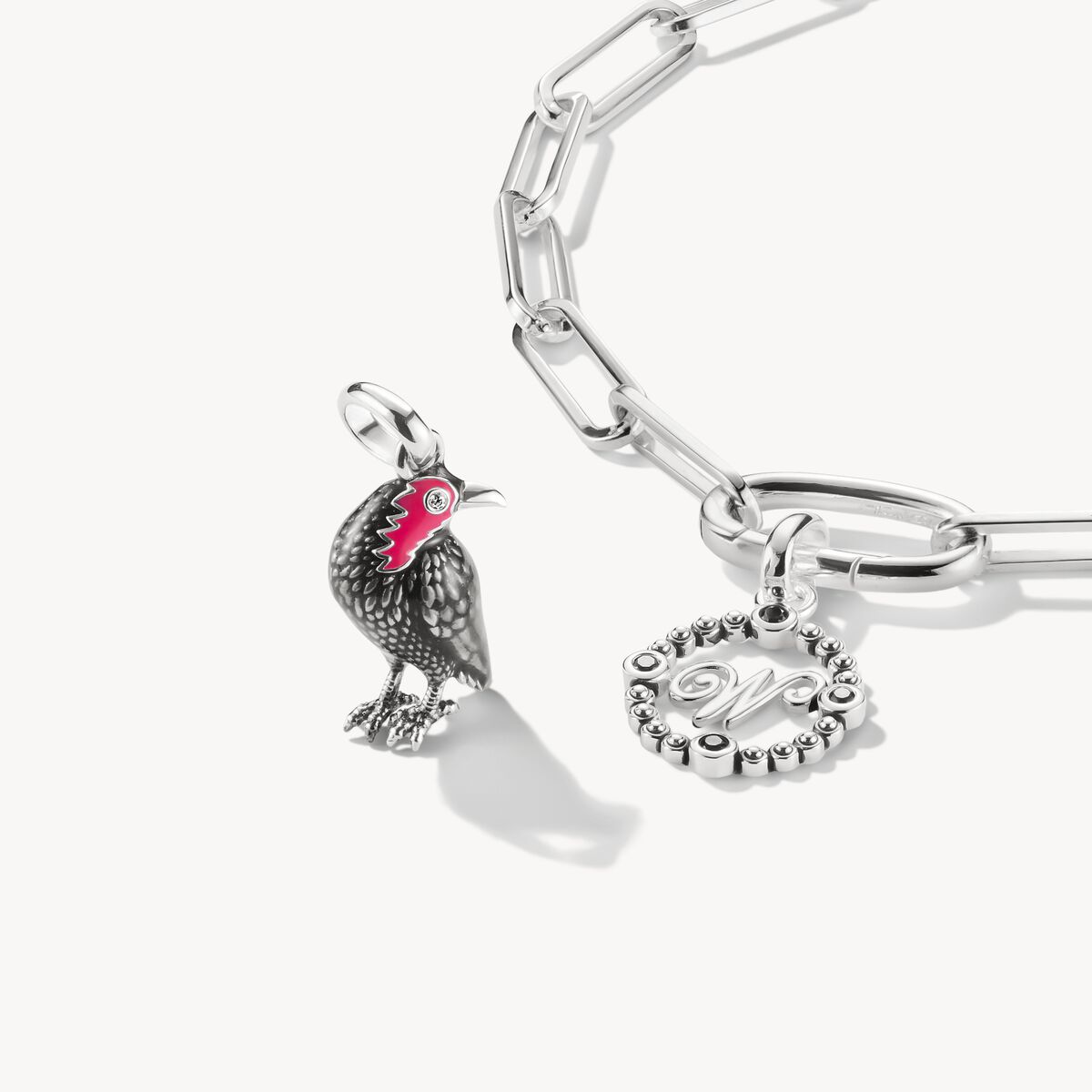 Silver bracelet with rooster charm and heart-shaped charm on a white background