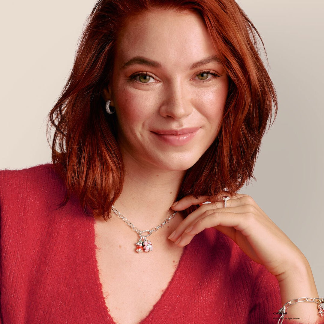 Woman wearing a red sweater and a necklace with a heart pendant against a neutral background