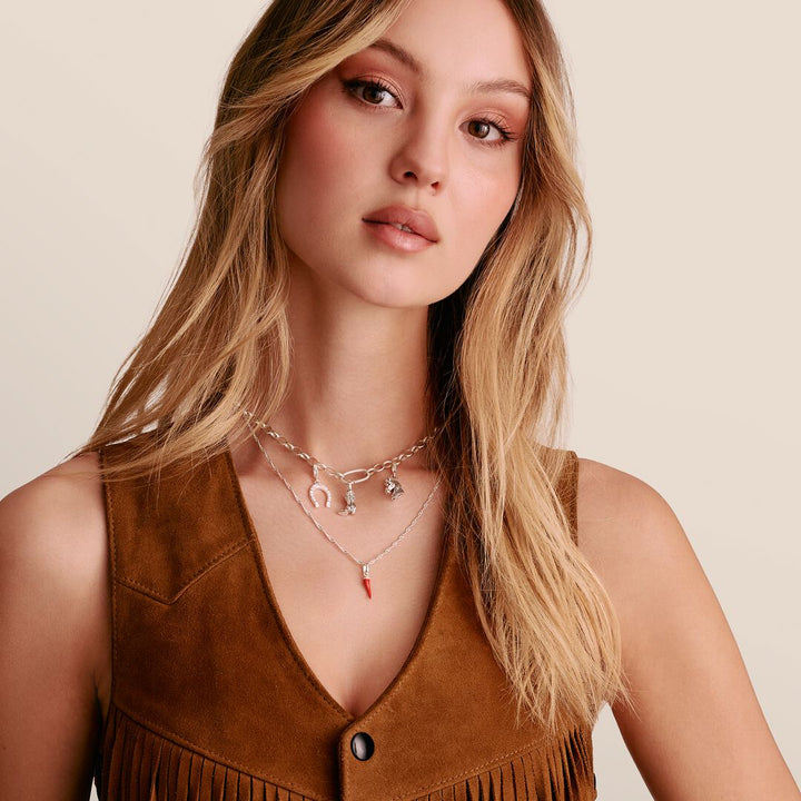 Woman wearing a brown suede vest with layered necklaces on a beige background