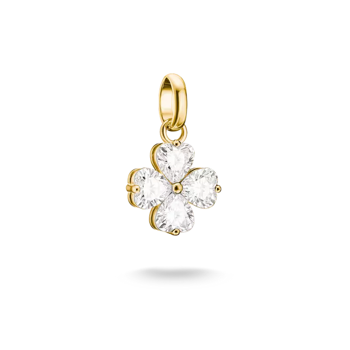 A gold four-petal flower charm pendant with clear heart-shaped gemstones, shown against a plain white background with a soft shadow underneath.