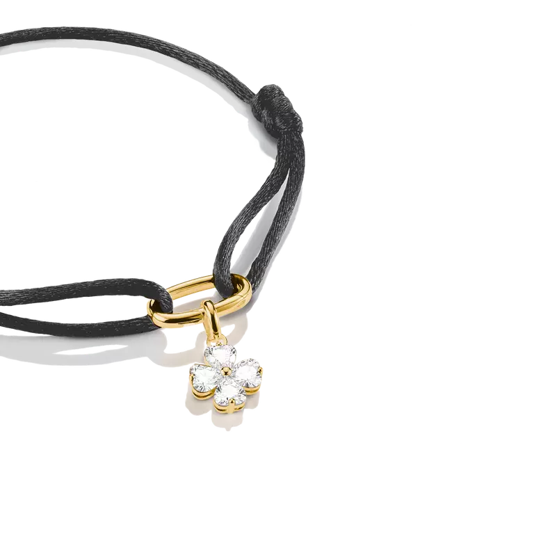 A black cord bracelet with a gold-tone clasp and a small flower-shaped clear gemstone charm, photographed on a clean white background.
