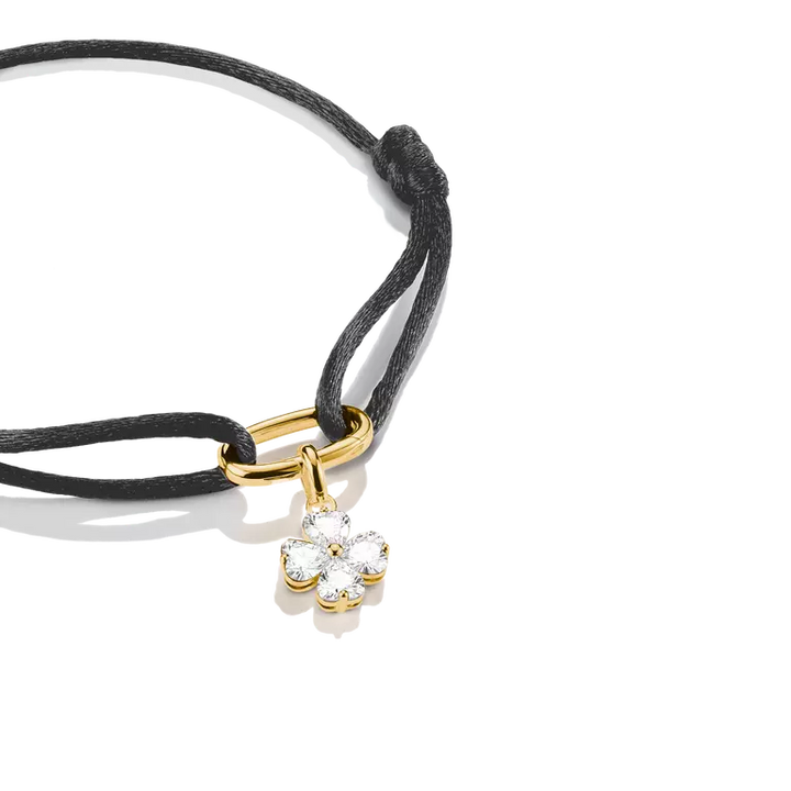A black cord bracelet with a gold-tone clasp and a small flower-shaped clear gemstone charm, photographed on a clean white background.