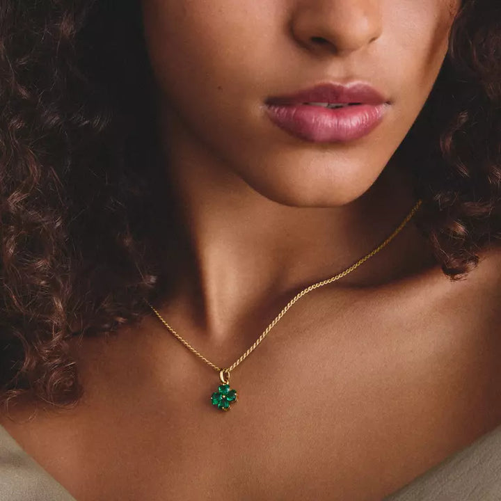 A close-up of a model wearing a delicate gold chain necklace with a small green clover-shaped pendant.