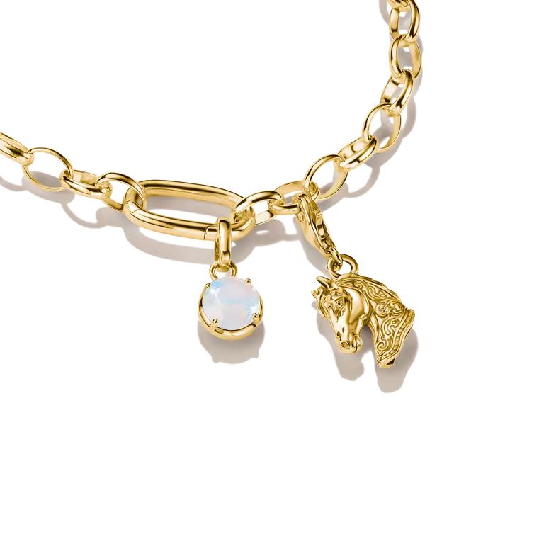 Gold chain bracelet featuring a large oval link charm, a small horse head charm, and a round white opal-like gemstone charm, shown on a clean white background.