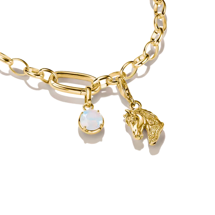 Gold chain bracelet featuring a large oval link charm, a small horse head charm, and a round white opal-like gemstone charm, shown on a clean white background.