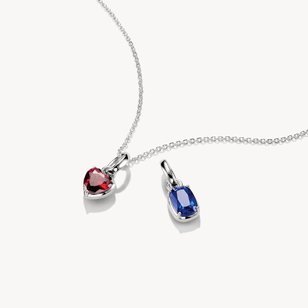 Two heart-shaped gemstone pendants on a chain against a white background