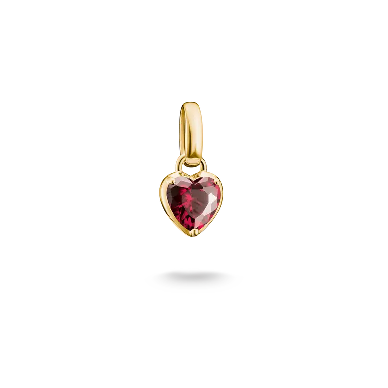 A gold heart-shaped pendant charm featuring a faceted dark pinkish-red gemstone, shown against a solid white background with a soft shadow underneath.