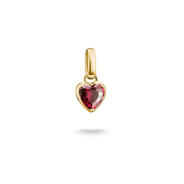 A gold heart-shaped pendant charm featuring a faceted dark pinkish-red gemstone, shown against a solid white background with a soft shadow underneath.