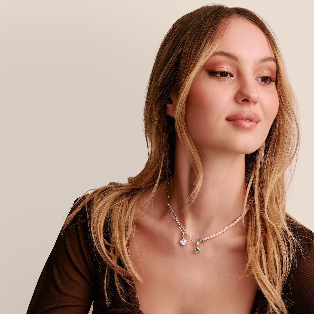 Woman wearing a necklace with a green gemstone against a neutral background