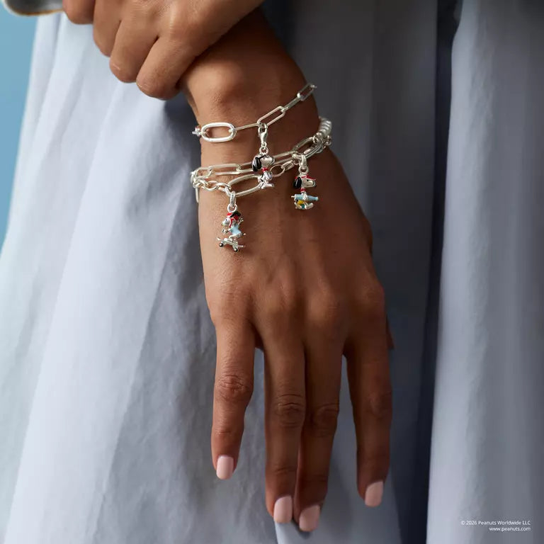 Hand wearing multiple silver bracelets with charms against a neutral background