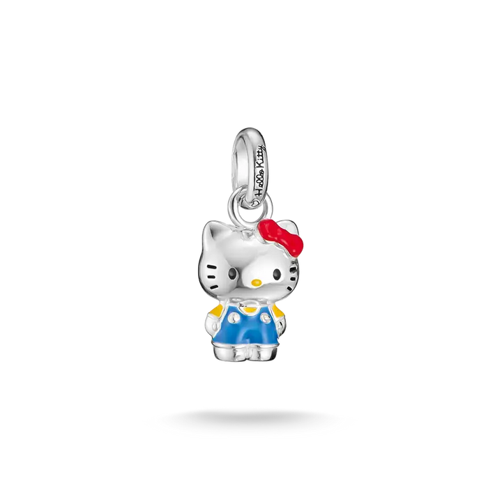 A silver Hello Kitty charm pendant featuring a silver body, blue overalls, a red bow, and yellow accents, shown on a clean white background with a soft shadow below.