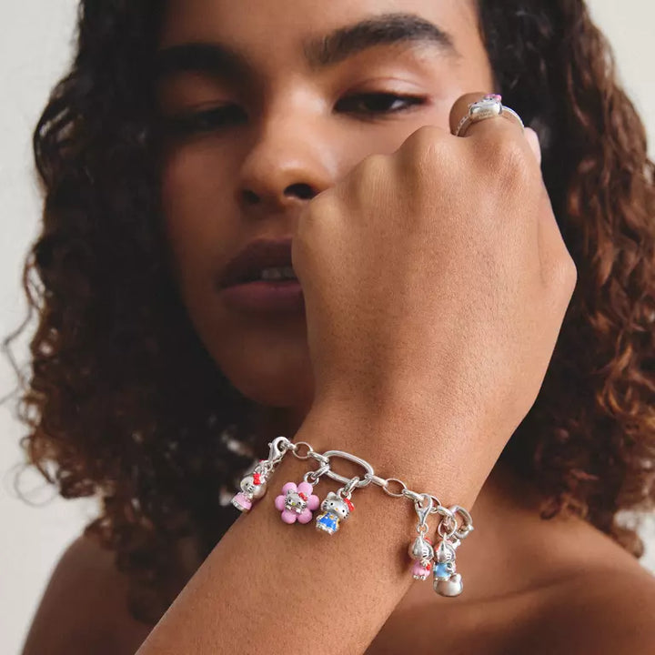 A close-up lifestyle shot of a model wearing a silver charm bracelet with colorful flower charms on her wrist, along with a silver ring on her finger.