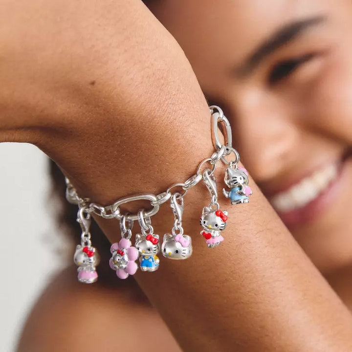 A silver chain bracelet with multiple dangling Hello Kitty charms and pink flower charms, shown worn on a person's wrist with a blurred smiling face in the background.