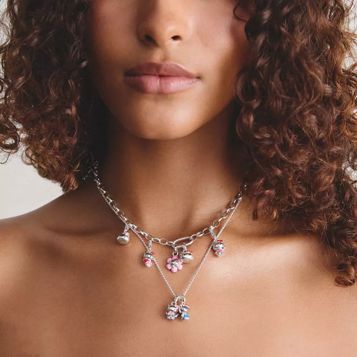 A close-up of a model wearing a silver-toned multi-strand charm necklace with pink and blue rhinestone accents.