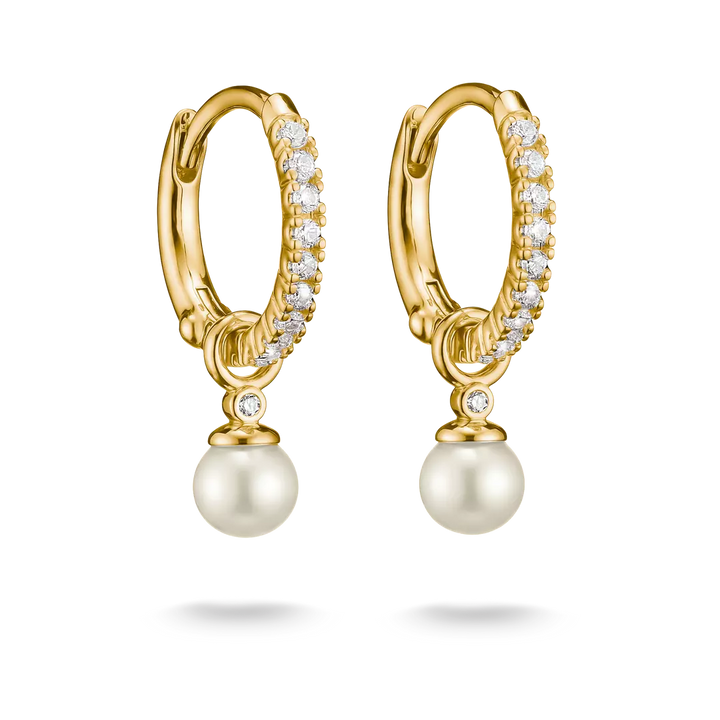 A pair of gold huggie hoop earrings with pavé-set clear stones and a dangling white pearl, shown on a clean white background.