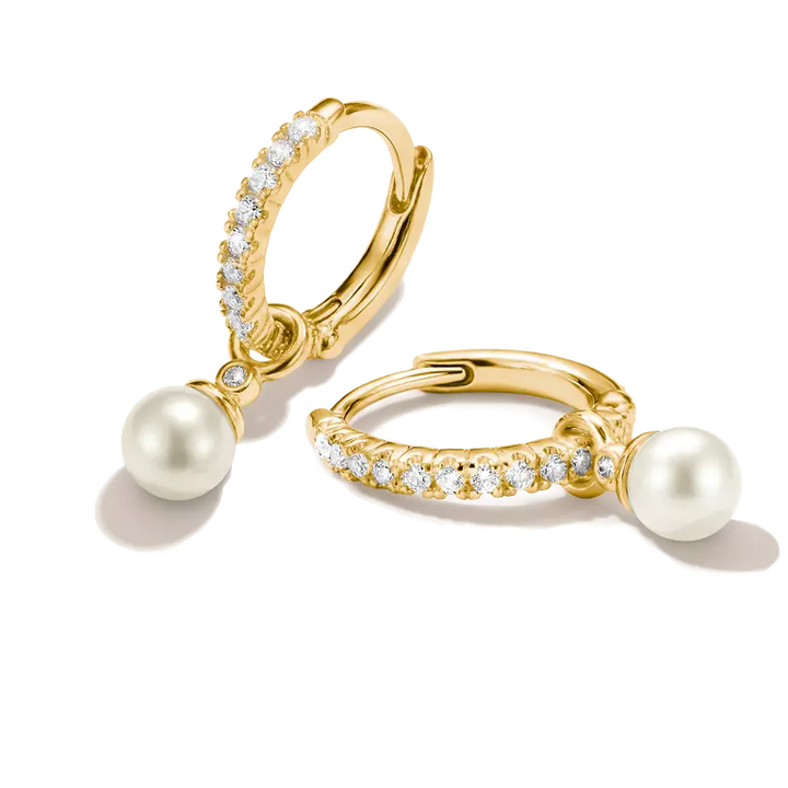 A pair of gold huggie hoop earrings with white freshwater pearls and rows of clear pavé stones, shown on a clean white background.
