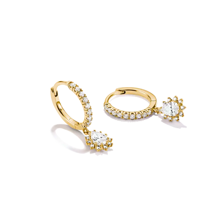 A pair of gold huggie hoop earrings with small clear stones along the outer curve and a dangling heart-shaped clear stone cluster at the bottom, shown on a white background.