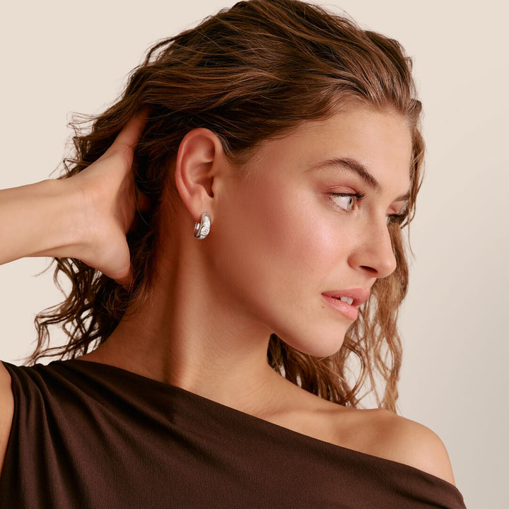 Woman wearing a silver earring with a neutral background