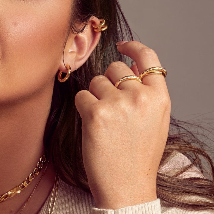 Close-up of a person wearing gold hoop earrings and rings 