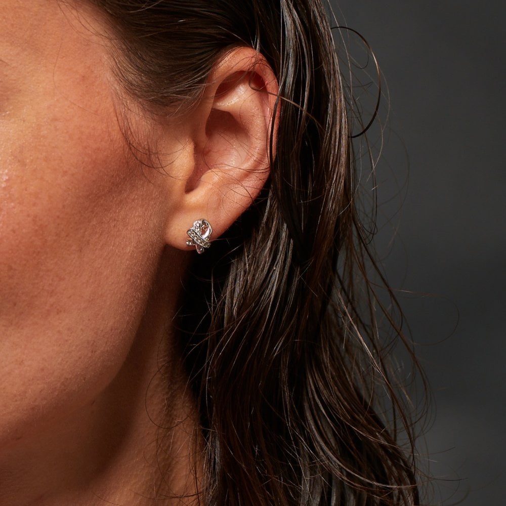 Close-up of an ear wearing a diamond earring with dark hair and skin background