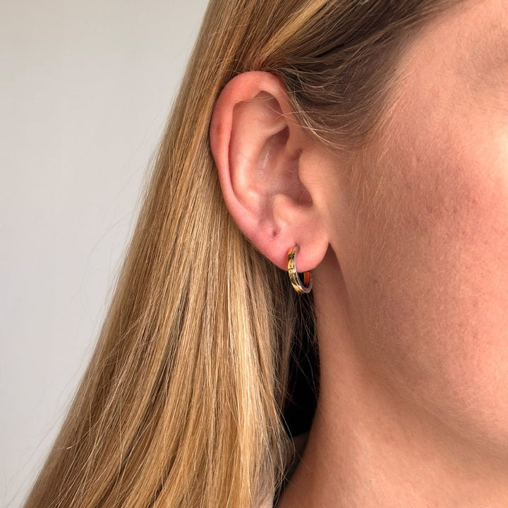 Close-up of an ear wearing a colorful hoop earring with blonde hair.