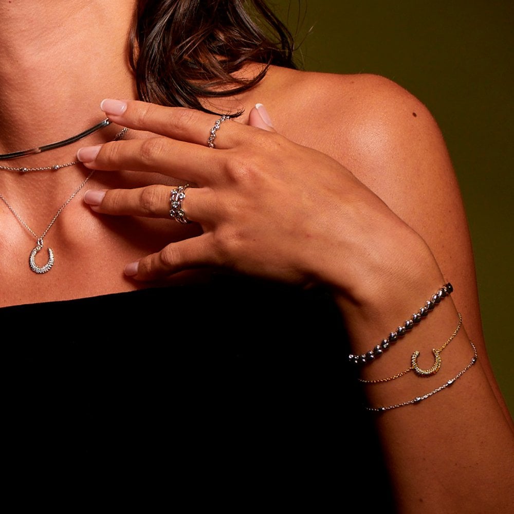 Close-up of a person wearing multiple necklaces, bracelets, and rings 