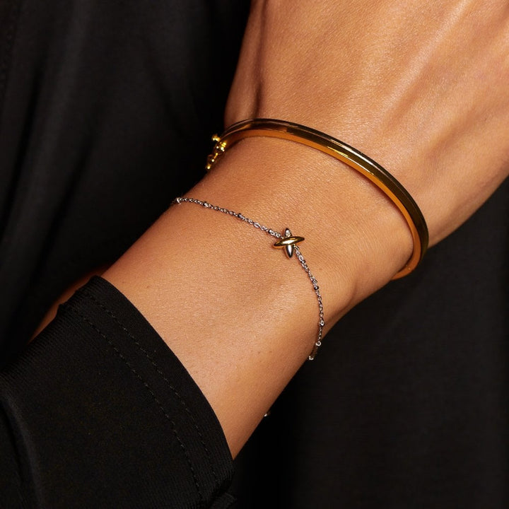 Close-up of a wrist wearing a gold bracelet and a silver star anklet 