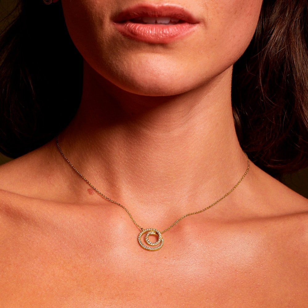 Close-up of a woman wearing a gold necklace with a circular pendant.