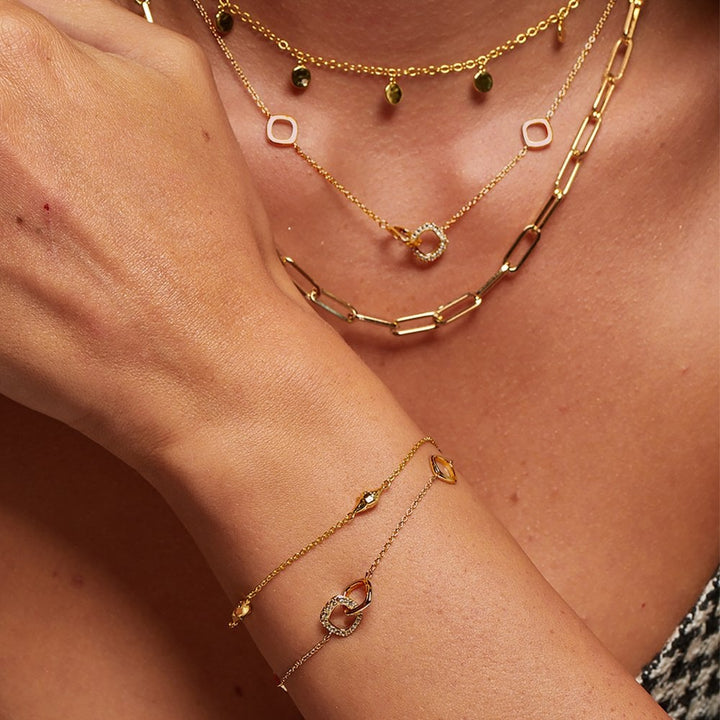 Close-up of a person wearing multiple gold necklaces and a bracelet 